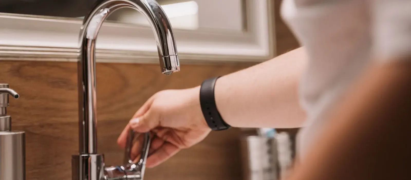 Hand adjusting the handle of a chrome gooseneck kitchen faucet