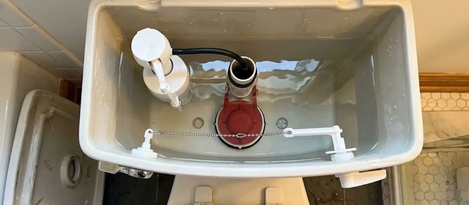 Open toilet tank showing the fill valve, red flapper and chain from above
